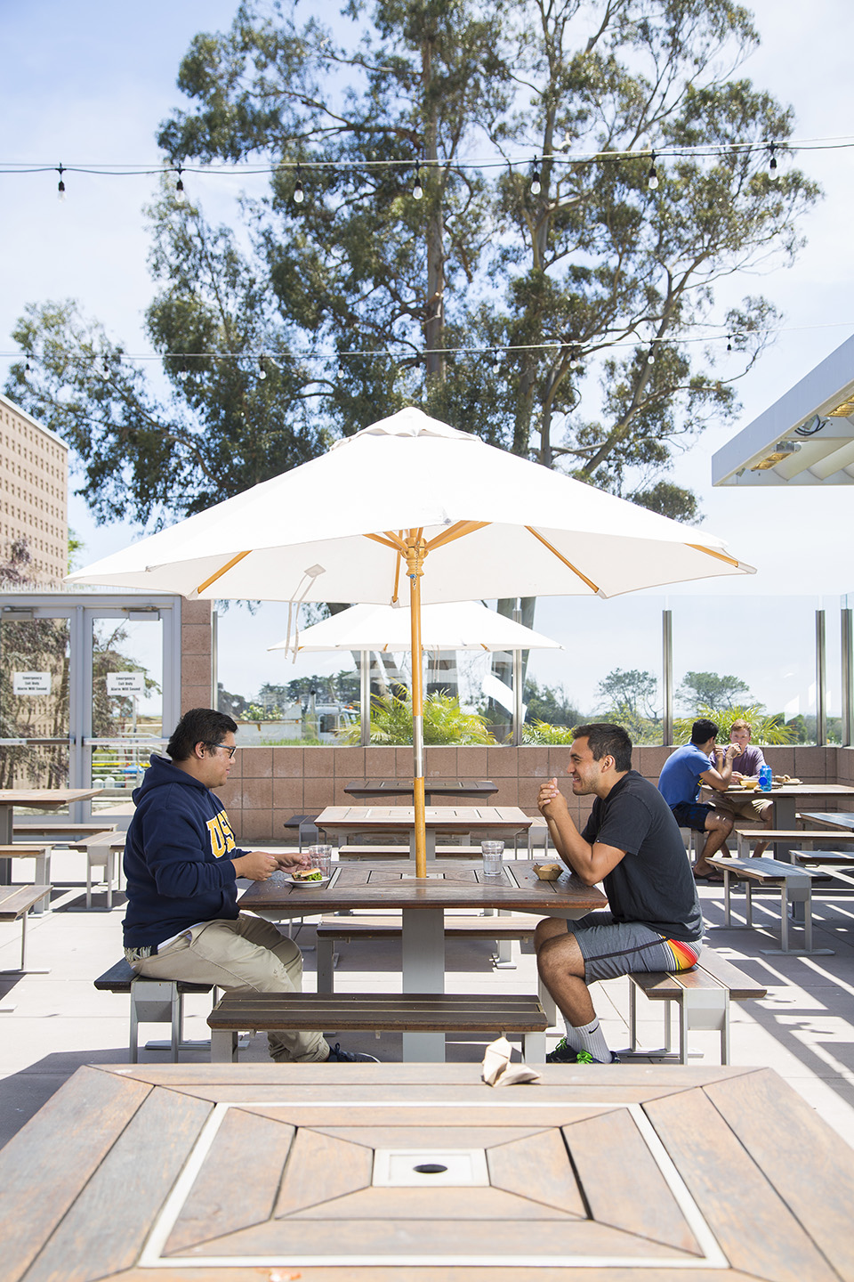 Two male students dining under umbrella on UCen deck